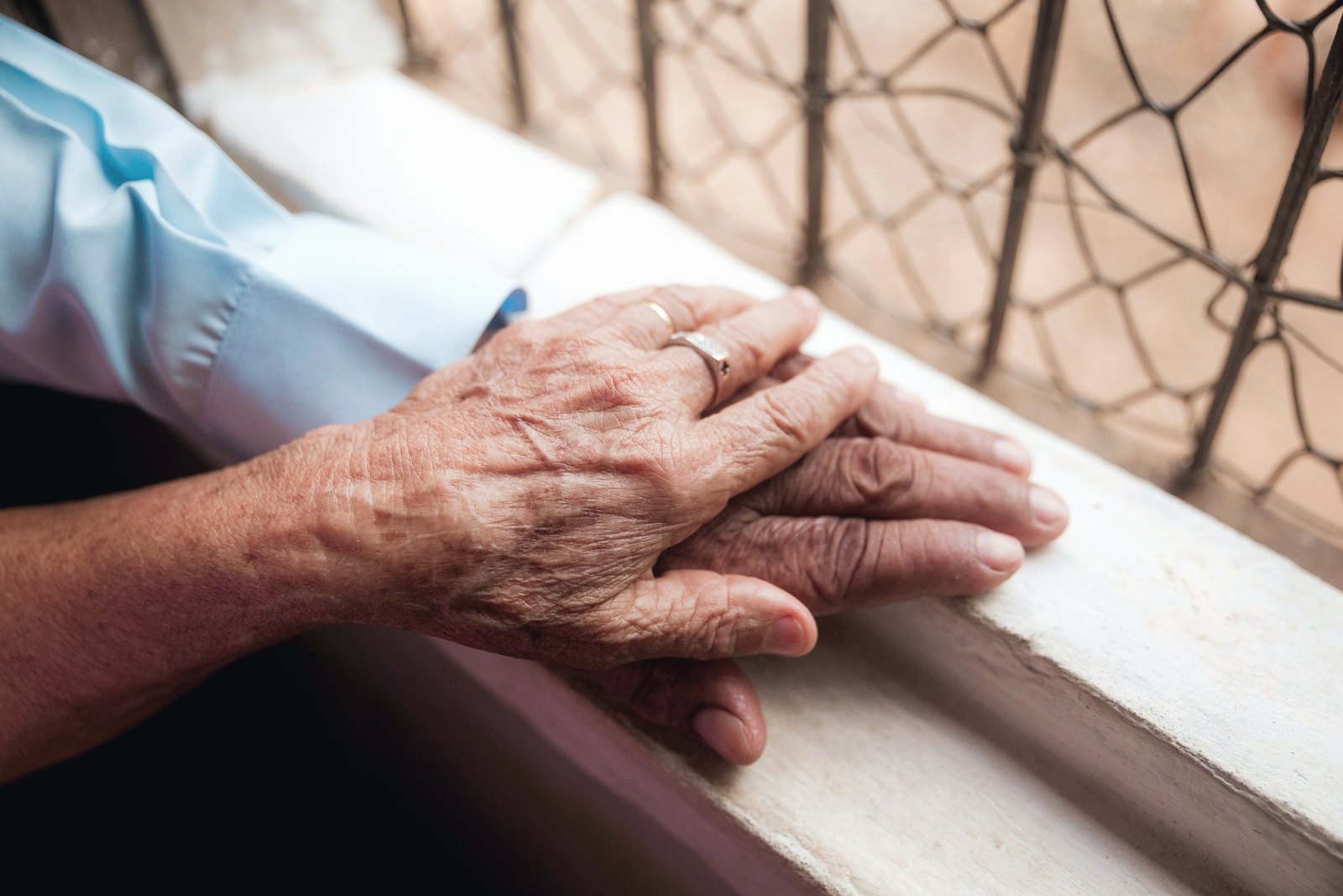 Two hands resting together on a windowsill, illustrative image
